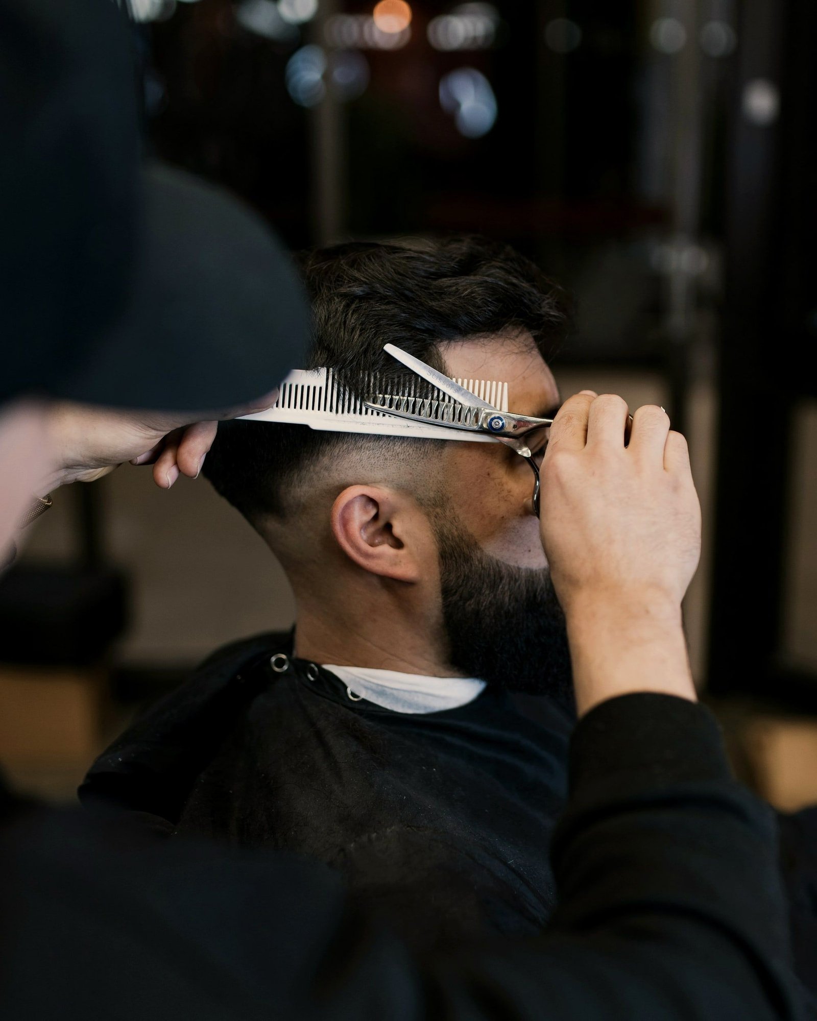 Maestro barbero corta a tijera sobre peine el cabello de un cliente