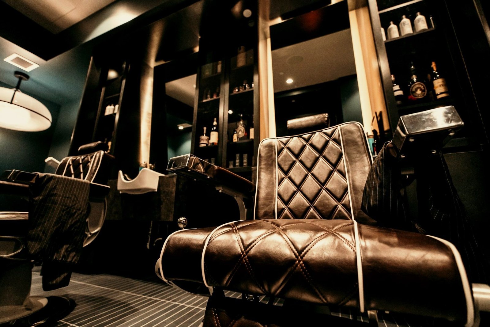 Sillón de barbero capitonado en piel junto al espejo en el salón de Sharp & Sleek