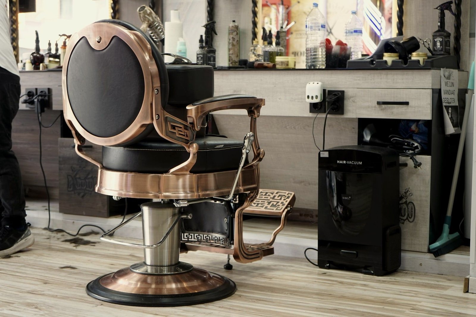 Sillón de barbero en piel negra con estructura de bronce frente al espejo